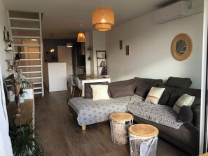 A modern living room with a sectional sofa, two round side tables, a dining area with a table and chairs, and a staircase leading to an upper level. - 🌞🪸 Le Corail 🪸 - Apartment 3 bedrooms 6 people - 🦩 Le Grau Du Roi 🦩🌞 (Le Grau-du-Roi)