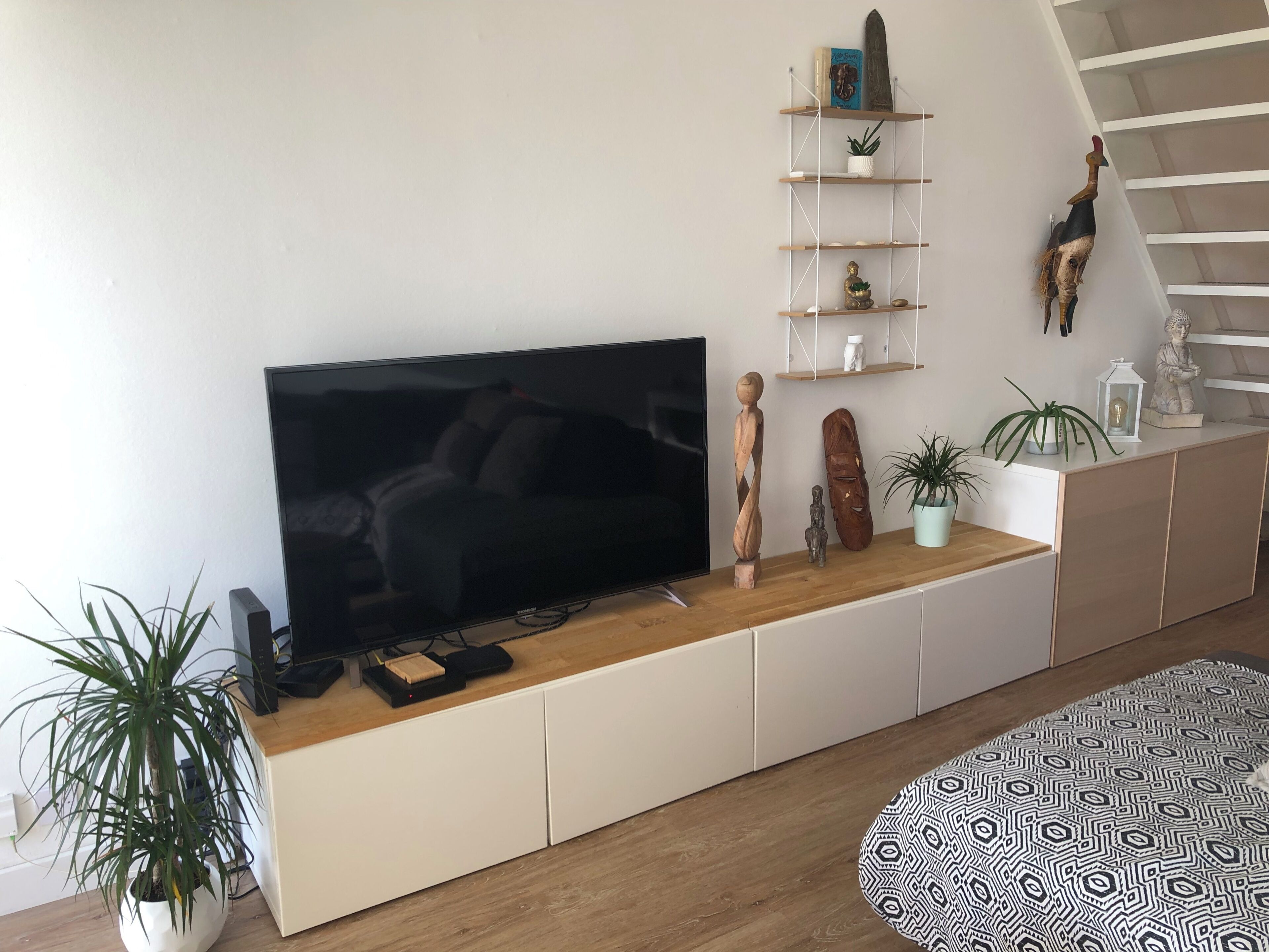 A modern living room with a flat-screen TV, wooden console, white cabinets, a staircase, and decorative items.