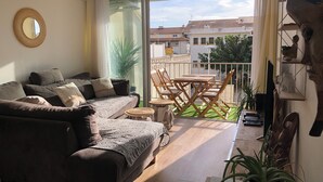 A modern living room with a sofa, a dining table with chairs, a hanging light fixture, and a view of the outside balcony. - 🌞🪸 Le Corail 🪸 - Apartment 3 bedrooms 6 people - 🦩 Le Grau Du Roi 🦩🌞 (Le Grau-du-Roi)
