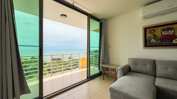 Una habitación con sofá gris, un cuadro en la pared y un balcón con vista al mar.