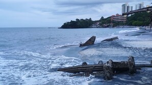 Una playa con olas, una estructura de madera y edificios al fondo.