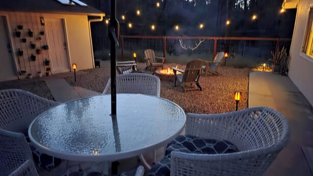 Une terrasse extérieure couverte, aménagée avec des meubles en osier, une table ronde et un foyer.