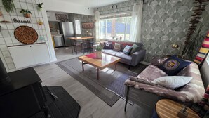 Un salon moderne avec un canapé, une table basse et un coin repas, la cuisine étant visible au fond.