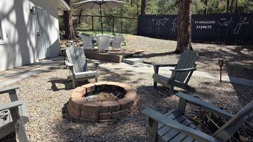 A backyard with a fire pit, Adirondack chairs, and a deck area.