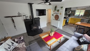 A modern living room with a fireplace, a TV, and a kitchen area with yellow cabinets.