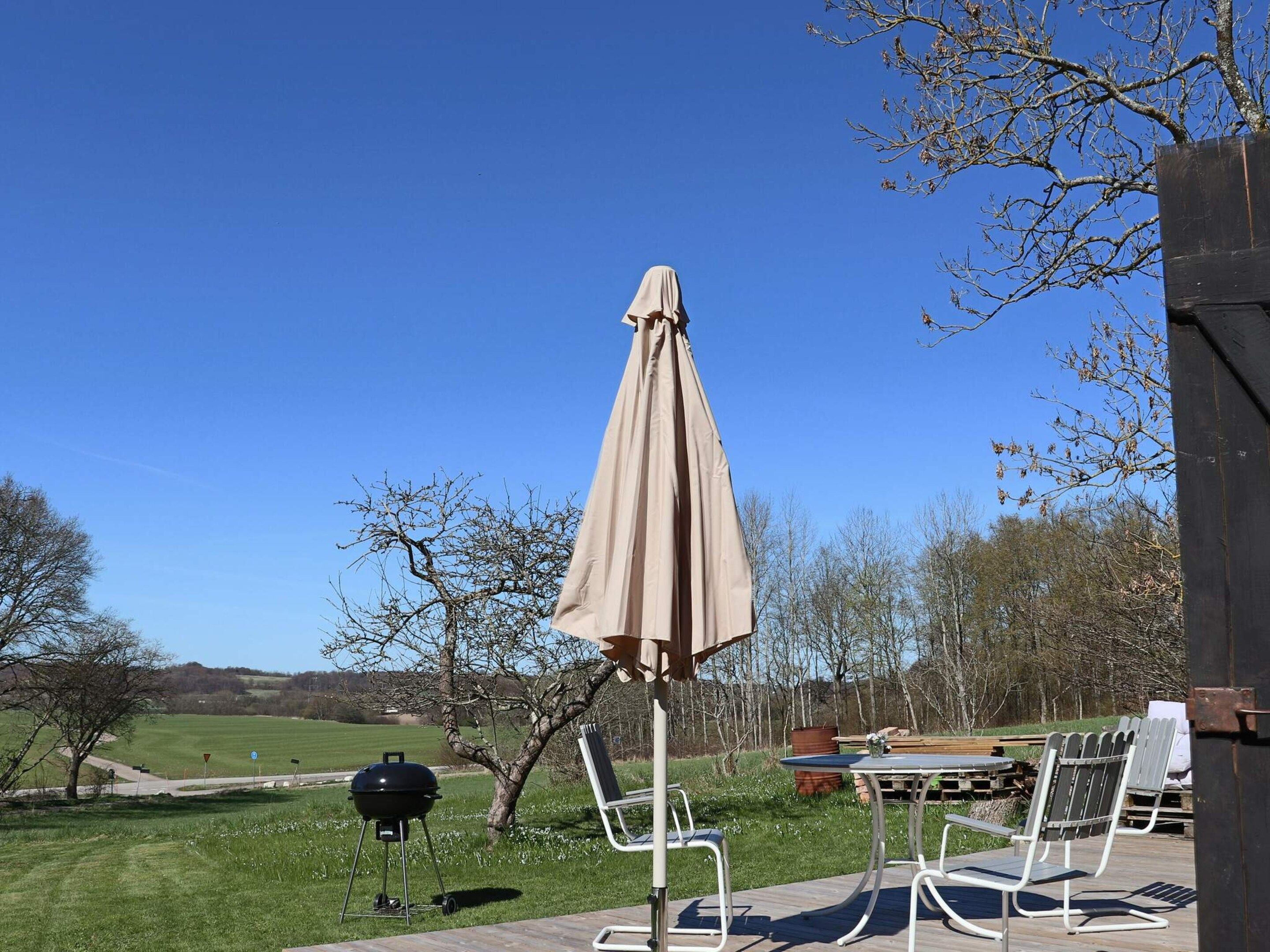 An outdoor patio with a grill, chairs, and an umbrella.