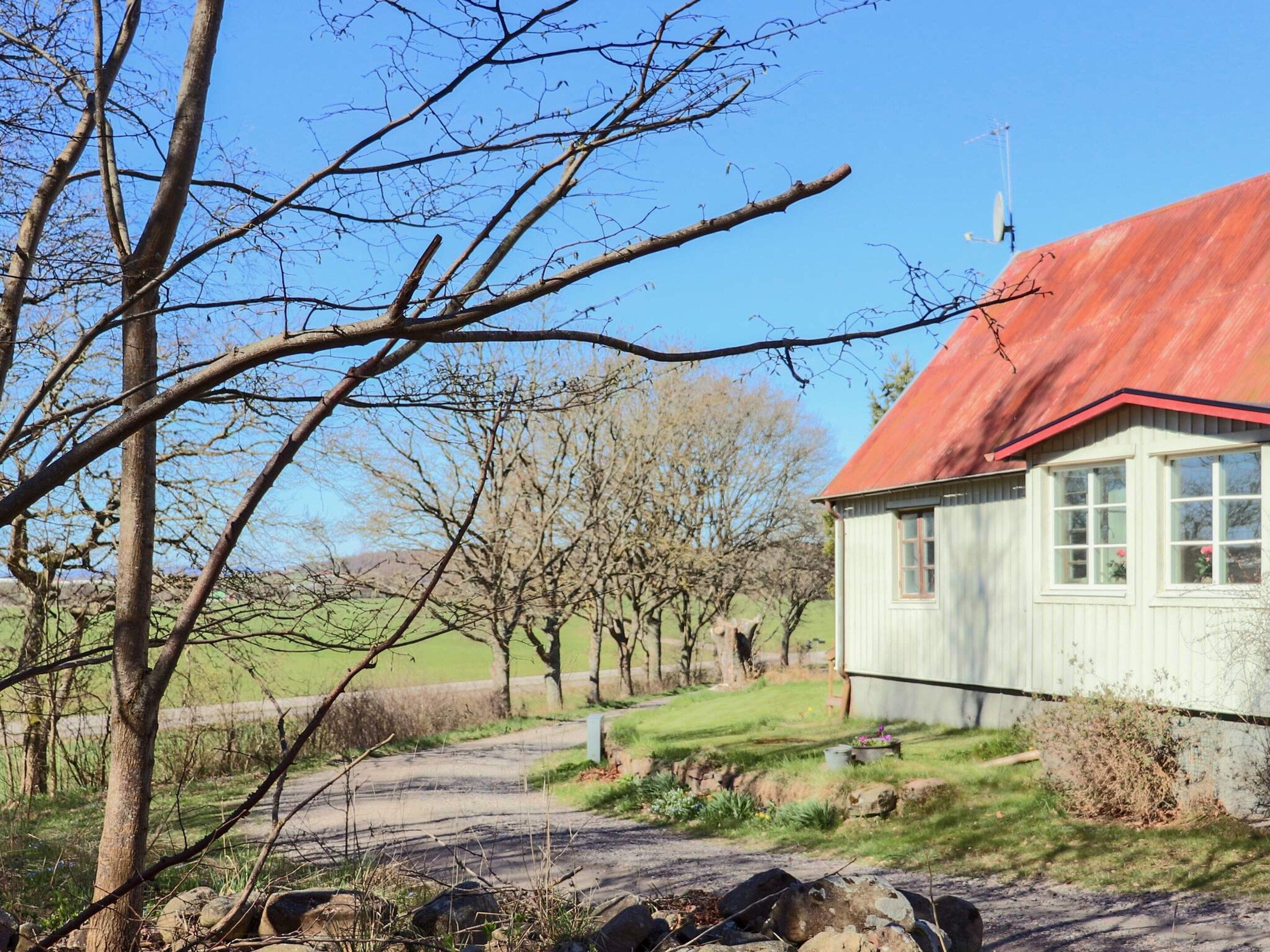 A rural setting with a house featuring a red roof, a clear sky, and a dirt path leading to the house.