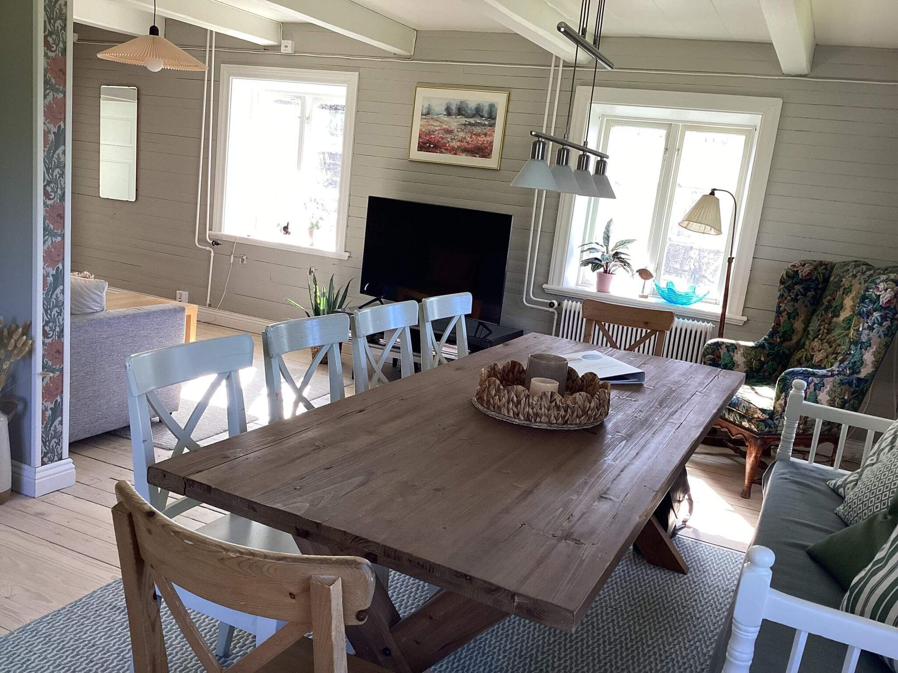 Un comedor con mesa de madera, sillas blancas y chimenea.