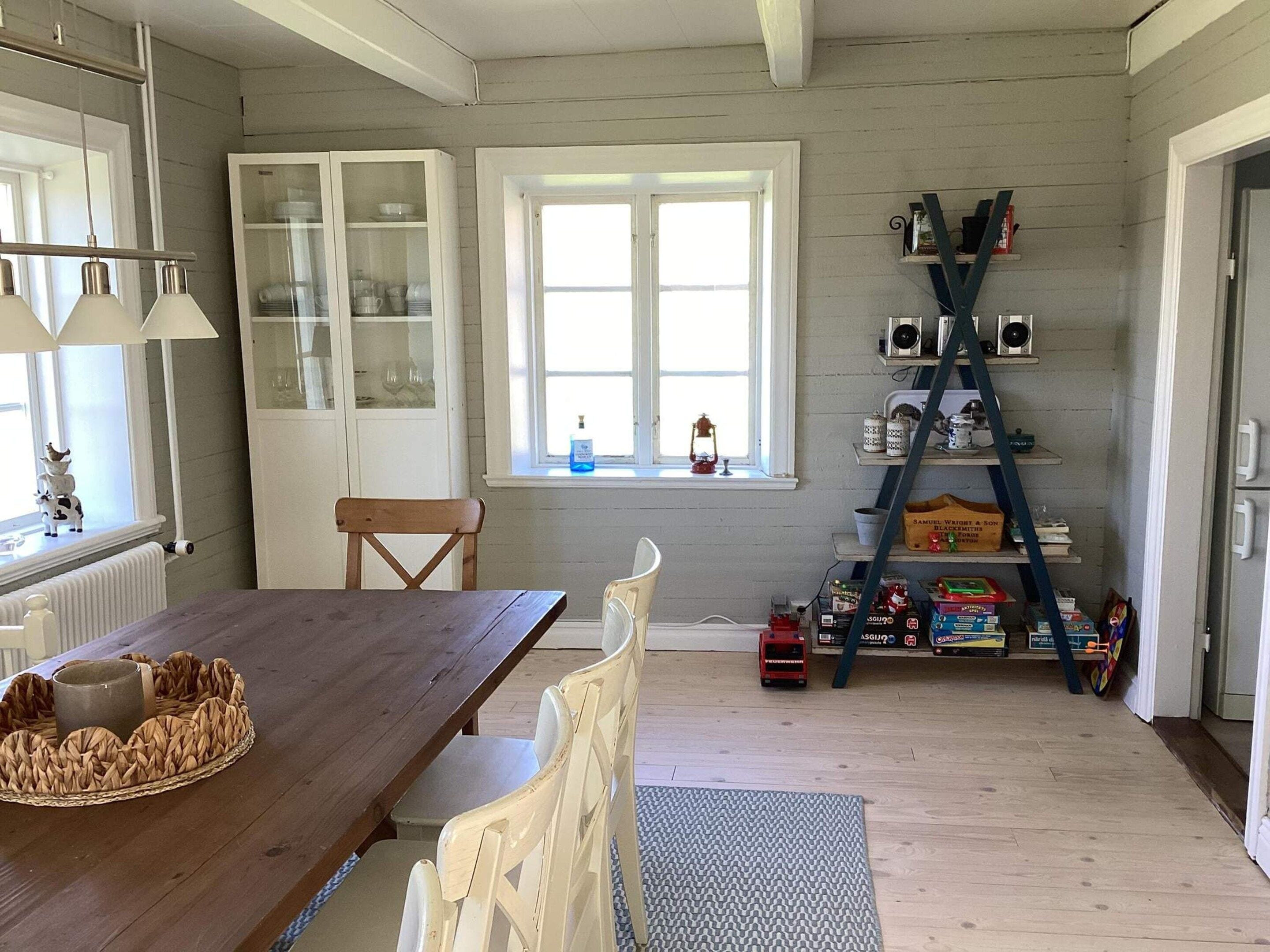 Eine Küche mit einem Holztisch, Stühlen, einem Fenster und einem Sprossregal mit verschiedenen Gegenständen.