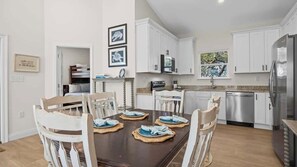 A modern kitchen with white cabinets, a dining table with chairs, and a refrigerator. - Fort Morgan House Beach Access 4 Bikes Sleeps 7! (Gulf Shores)
