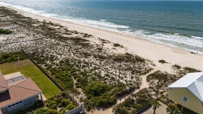 A beach with a paved walkway, a building with a sloped roof, and a clear view of the ocean. - Fort Morgan House Beach Access 4 Bikes Sleeps 7! (Gulf Shores)