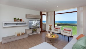 Una sala de estar moderna con televisor, muebles de madera, una mesa de centro y vista al océano.