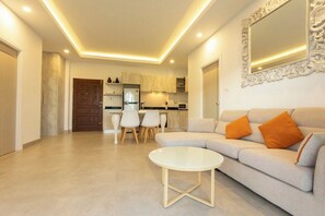 A modern living room with a sofa, a coffee table, and a dining area with chairs. - 2BR Walk Award Winning Beach Pool & Gym C126 (Tambon Rawai)