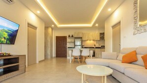 Una sala de estar moderna con un televisor de pantalla plana, una mesa de centro redonda y un sofá con cojines naranjas.