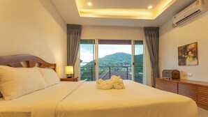 Habitación de hotel con una cama grande, una mesita de noche, una lámpara, un aparador de madera y vistas a la montaña a través de grandes ventanales.