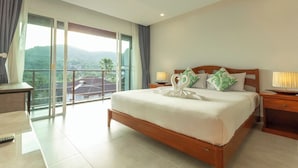 Habitación de hotel con una cama grande, cabecera de madera, mesita de noche con lámpara y balcón con vistas a zonas verdes.