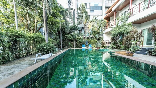 Una piscina con agua cristalina, rodeada de exuberante vegetación y edificios modernos.