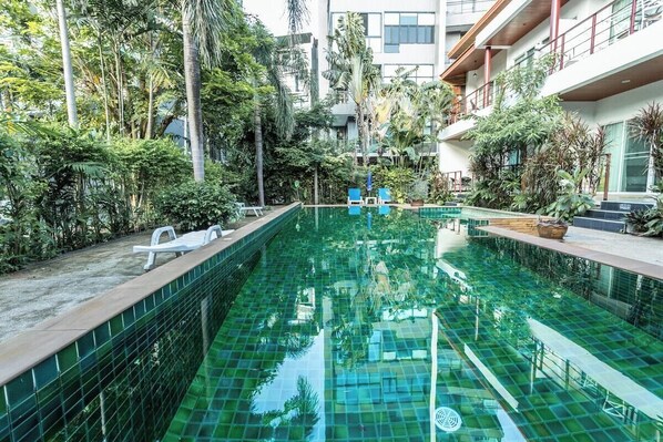 A swimming pool with clear water, surrounded by lush greenery and modern buildings. - 2BR Walk Award Winning Beach Pool & Gym C126 (Tambon Rawai)