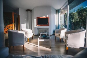Una sala de estar moderna con chimenea, un televisor de pantalla plana montado encima y ventanas amplias que ofrecen vistas a zonas verdes.