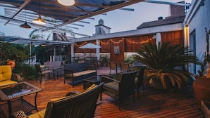 Un patio al aire libre con suelo de madera, mobiliario de mimbre e iluminación con guirnaldas.