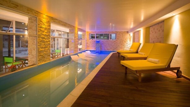 Una piscina interior con muelle de madera, sillones de descanso y pared de piedra.