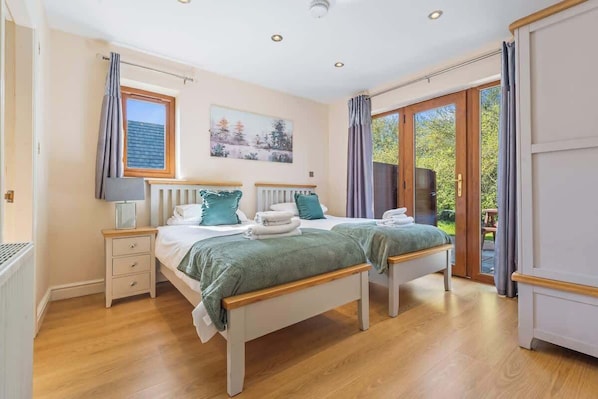 A bedroom with two beds, a window, a radiator, and a door leading to an outdoor area.