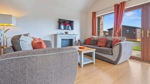Ein modernes Wohnzimmer mit Kamin, Flachbildfernseher und großem Fenster mit Vorhängen.