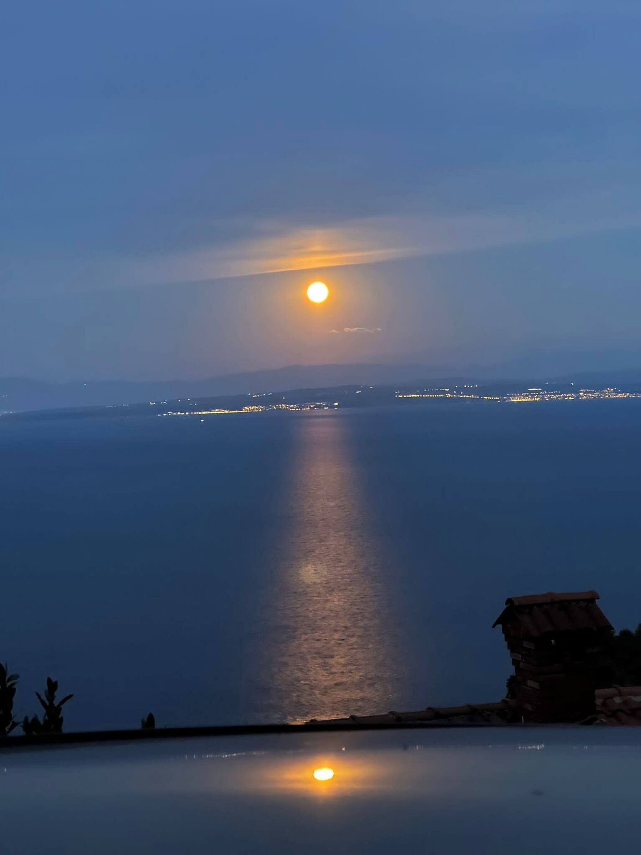 A sunset over a calm sea with distant city lights.
