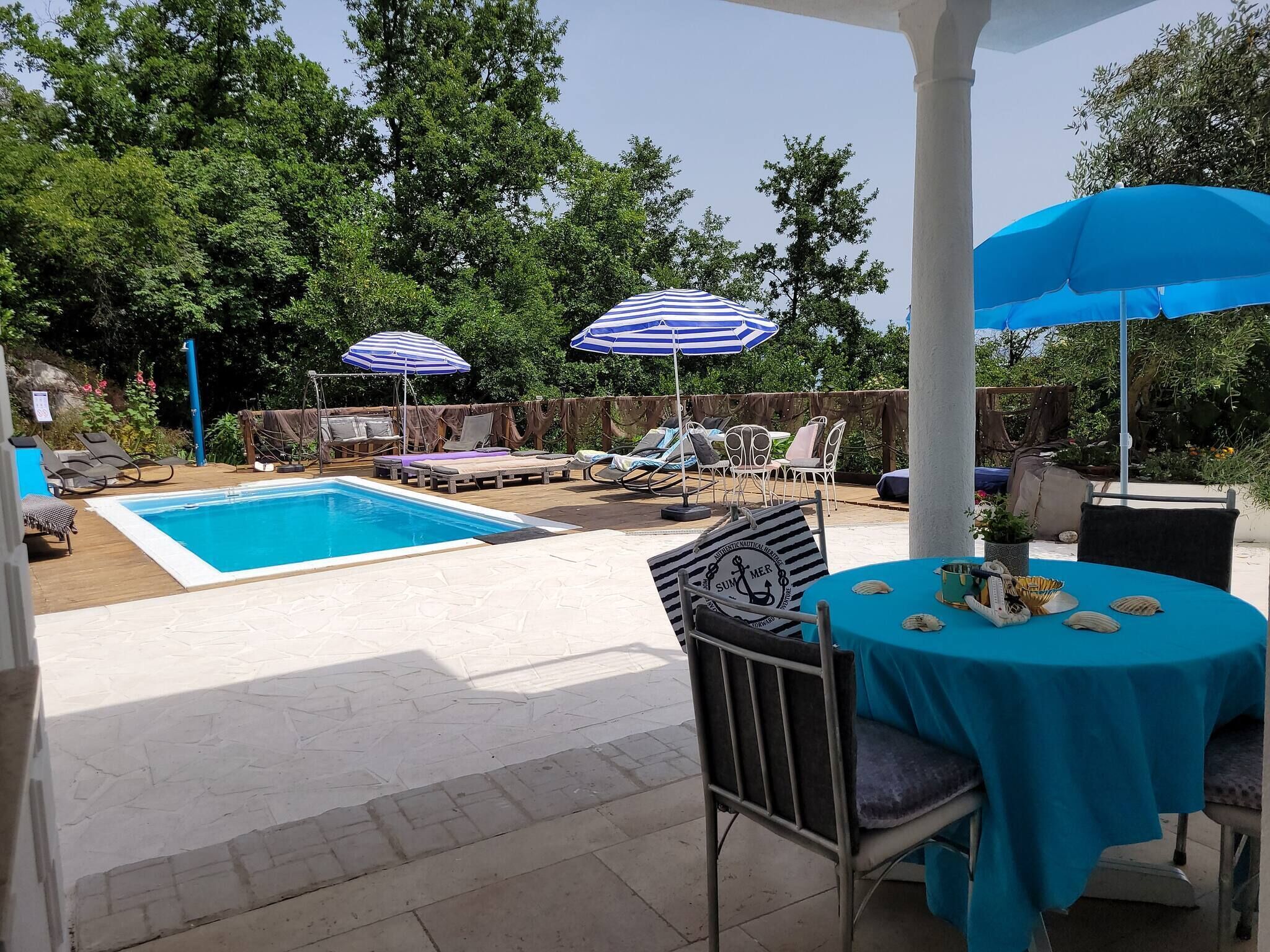 Uma área de piscina com espreguiçadeiras, guarda-sóis e uma mesa com toalha azul.