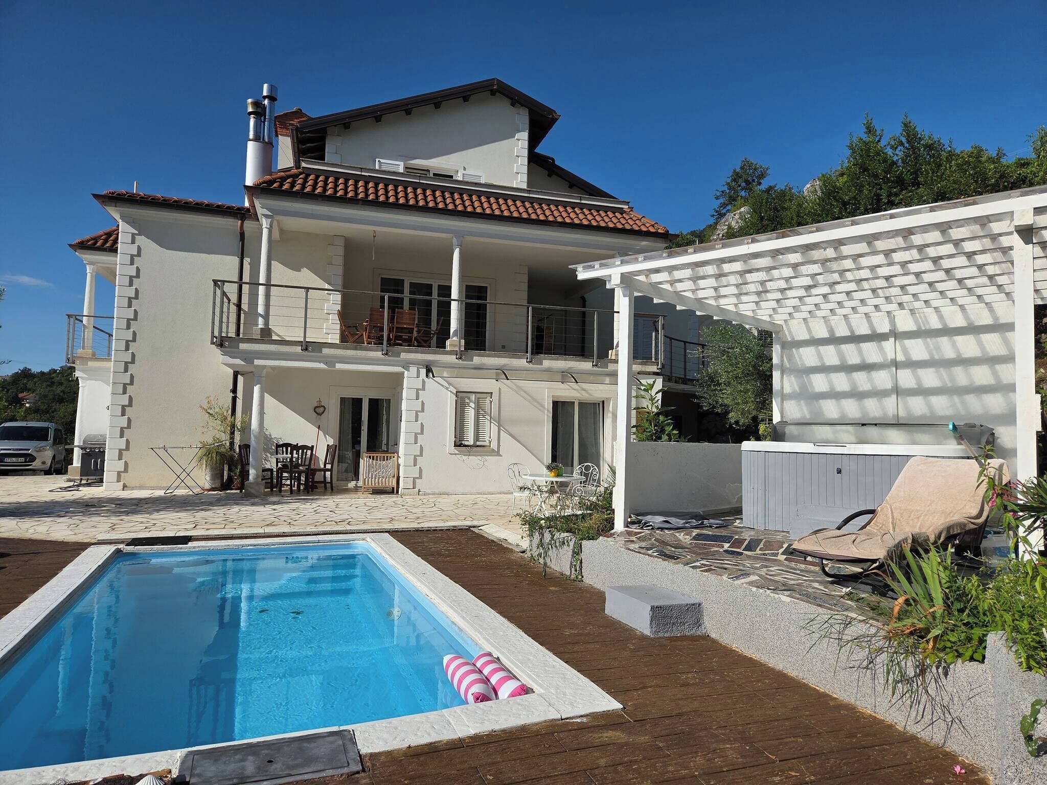 Una casa de dos plantas con piscina, mobiliario exterior y un patio cubierto.