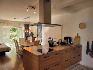 Une cuisine moderne dotée d’un îlot central, d’un coin repas avec une table et des chaises, et d’une grande fenêtre offrant une vue sur la verdure.