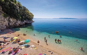 Una playa con agua cristalina, gente nadando y tomando el sol, y un acantilado rocoso.
