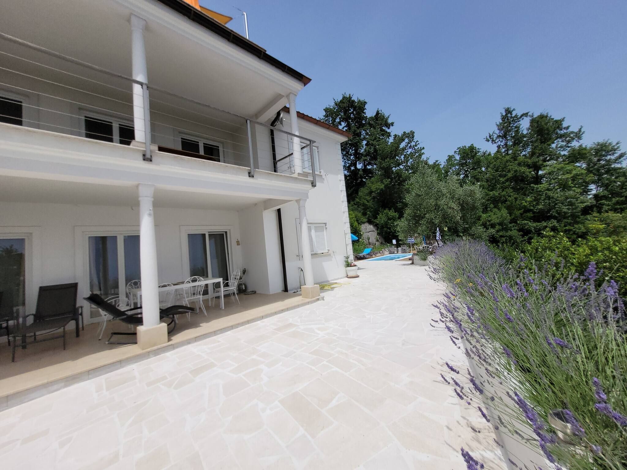 A two-story building with a balcony, a patio with outdoor furniture, and a swimming pool.