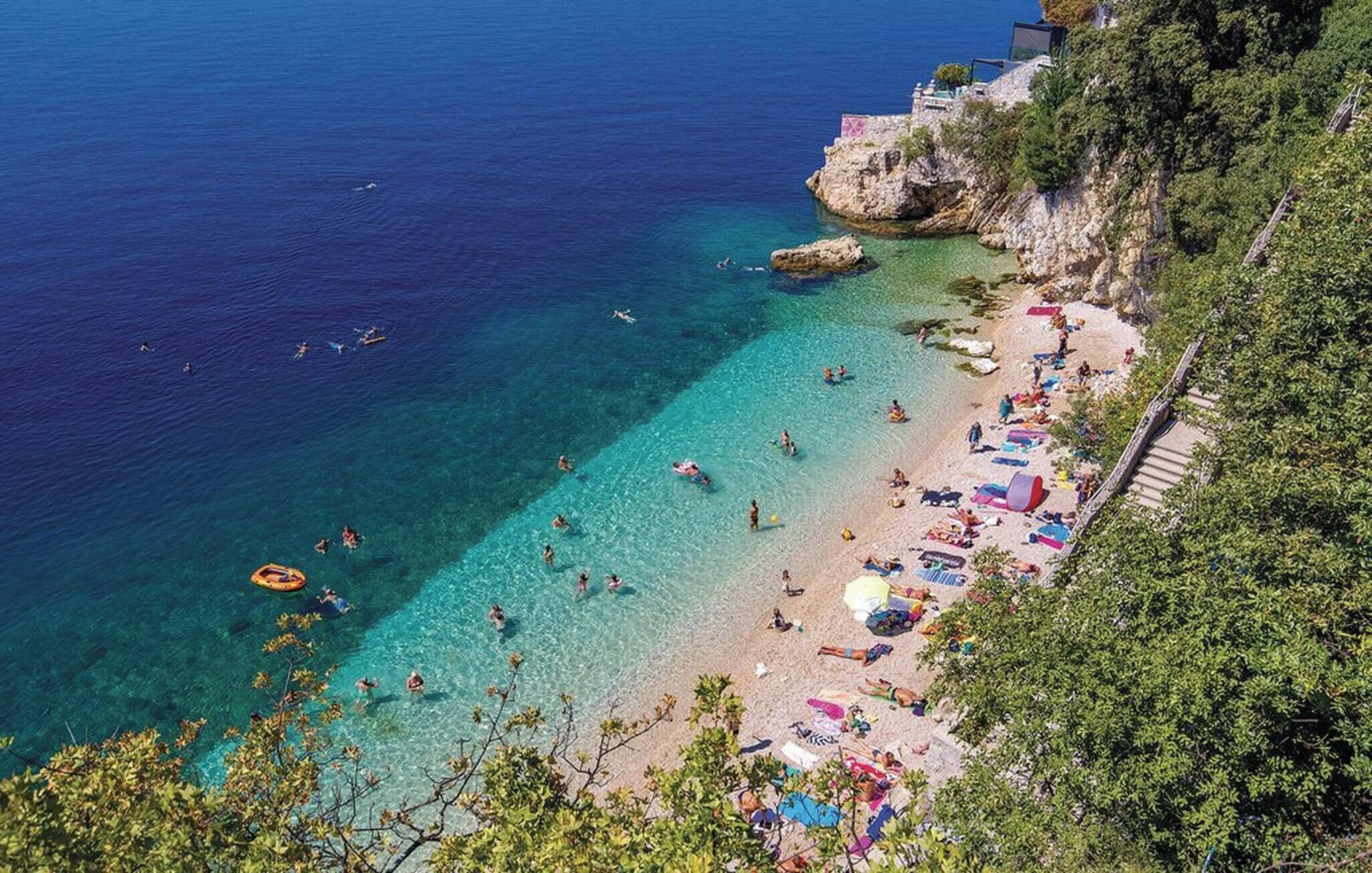 A coastal beach with clear waters, a rocky cliff, and a row of beach umbrellas.