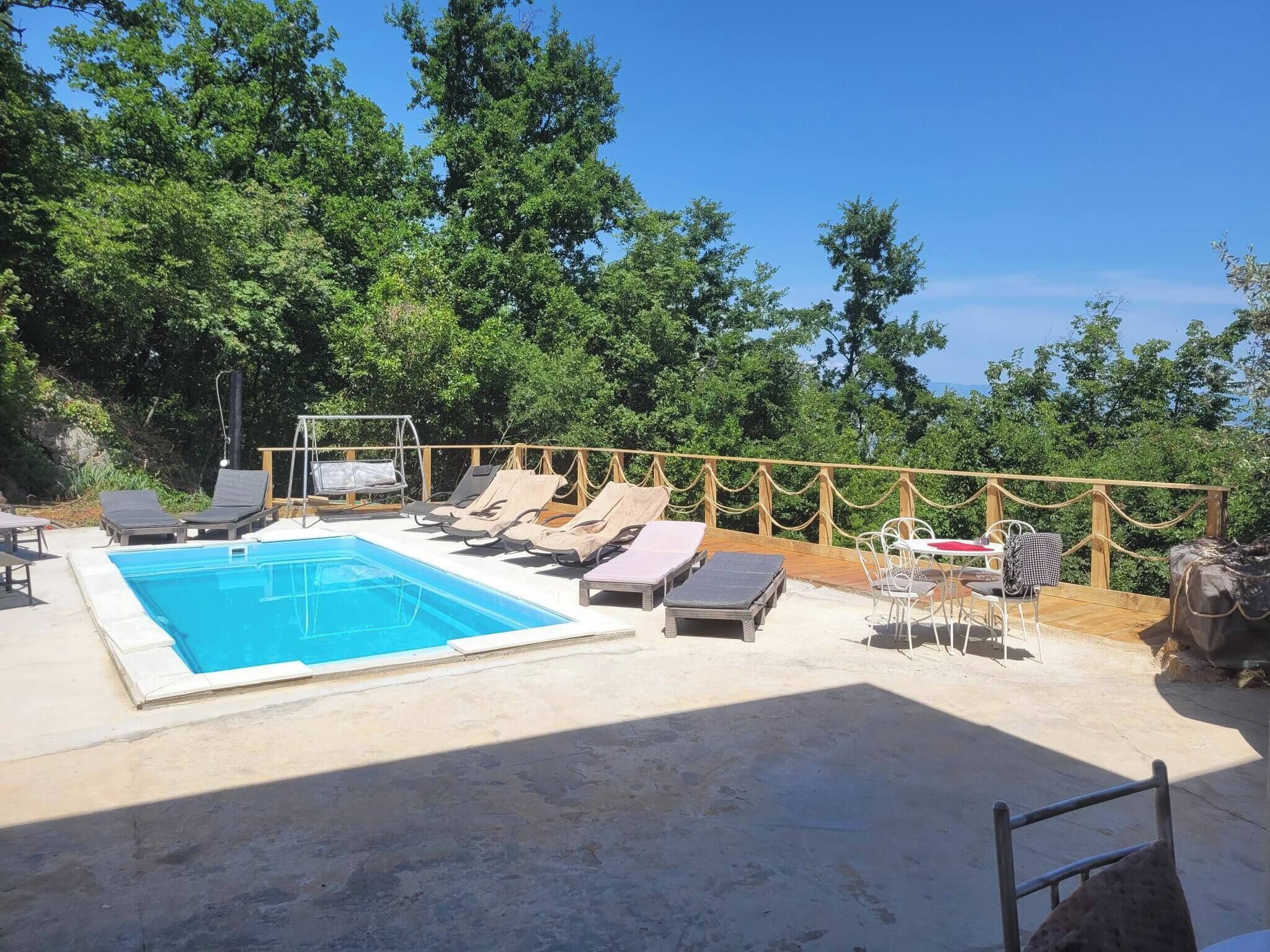 A swimming pool with lounge chairs and a table, surrounded by a wooden deck and trees.