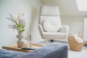 Ein stilvolles Wohnzimmer mit Hochstuhl, Blumen in einer Vase, Fernbedienung und einem gewebten Korb.