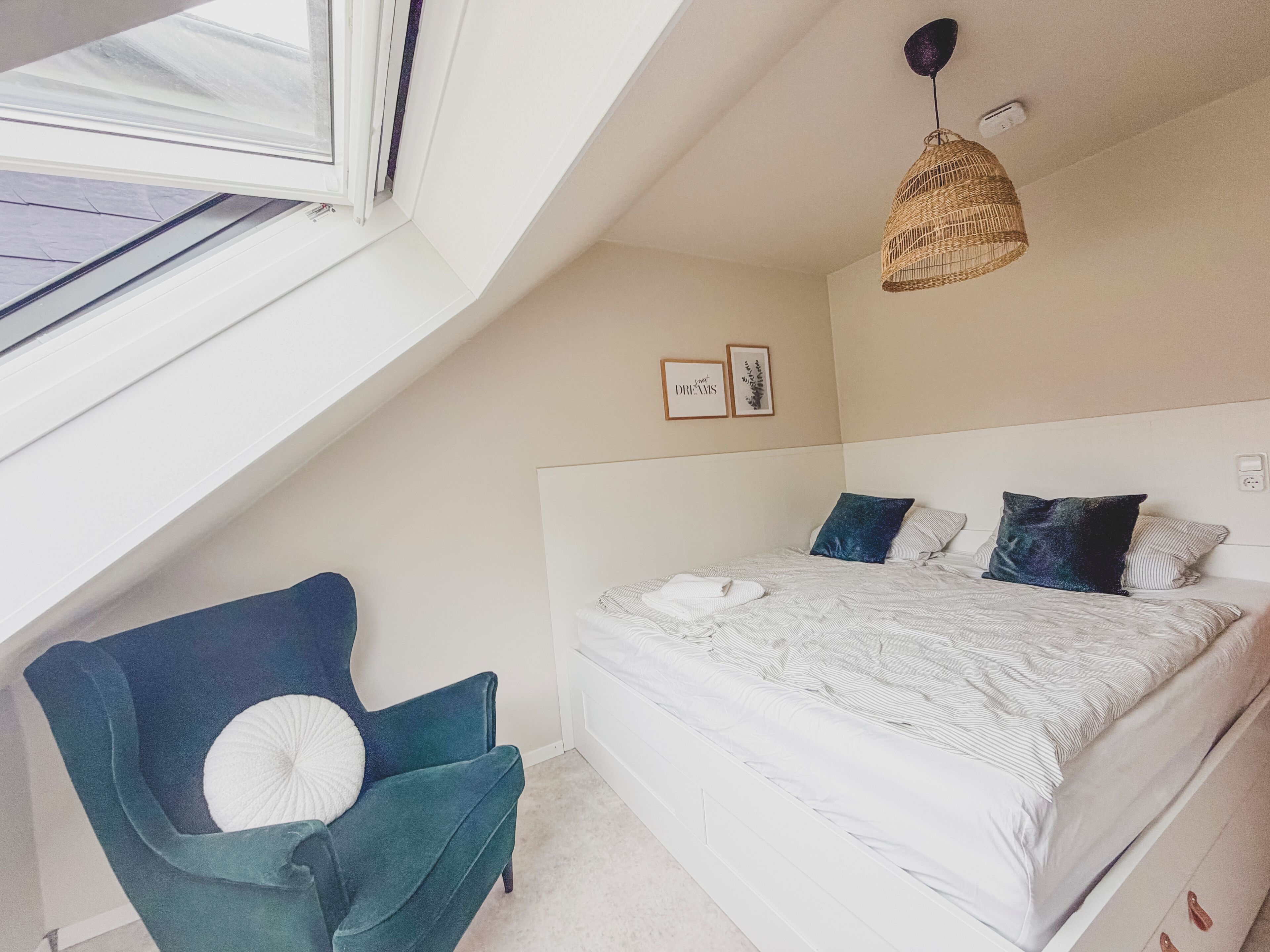 Une chambre à coucher avec un lit, une chaise, un luminaire suspendu et deux tableaux encadrés accrochés au mur.