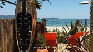 A wooden deck with two orange chairs, a potted plant, and a surfboard leaning against a wooden fence. - Residencial Pé na Areia Bombinhas (Bombinhas)