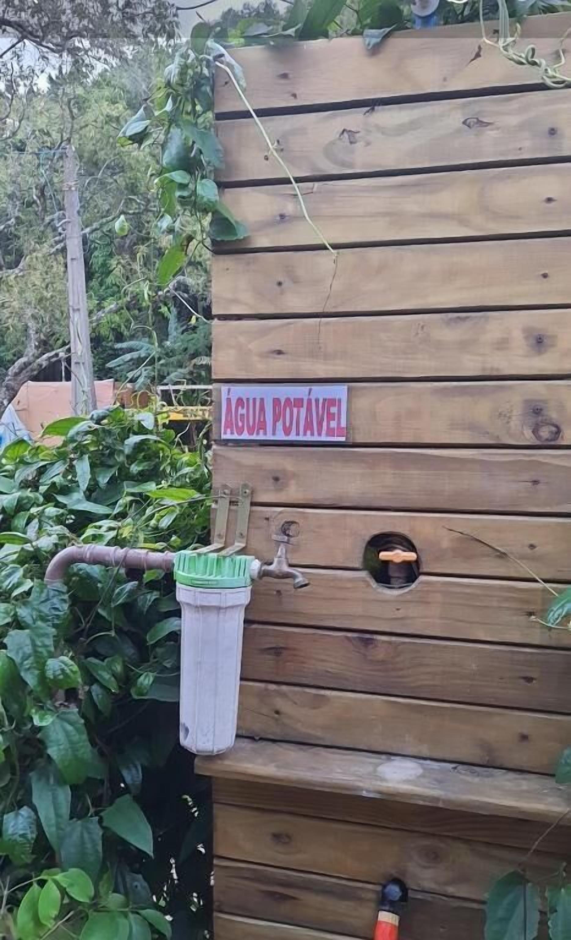 A wooden structure with a sign reading 'ÁGUA POTÁVEL' and a water spigot.