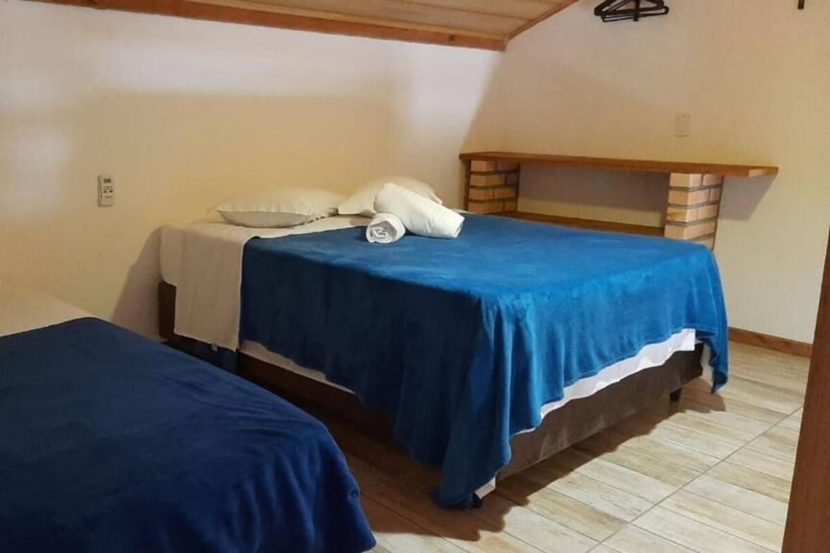 A room with two beds, each with a blue bedspread, a wooden headboard, and a small shelf.