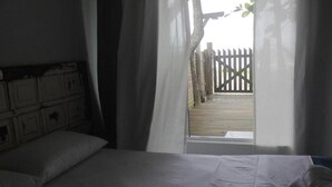 A bedroom with a bed, curtains, and a view of a wooden deck outside. - Residencial Pé na Areia Bombinhas (Bombinhas)