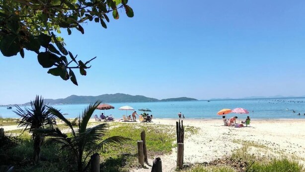 A beach with people, umbrellas, and a clear sky. - Residencial Pé na Areia Bombinhas (Bombinhas)