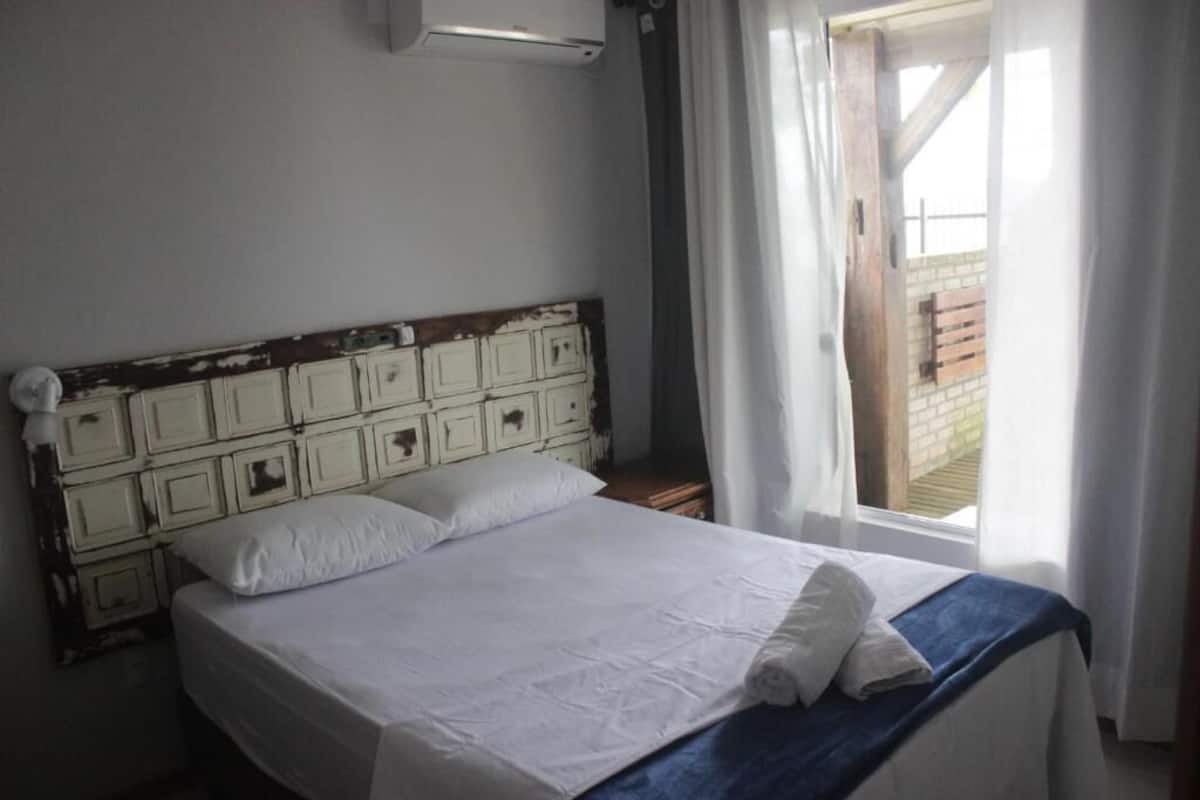 A bed with a white mattress and pillows, a wooden headboard, and a window with curtains.