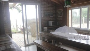 A room with a sliding glass door leading to a patio, a wooden bench, a table with a lace tablecloth, a microwave, and a hanging light fixture. - Residencial Pé na Areia Bombinhas (Bombinhas)