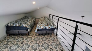 Um pequeno apartamento de um quarto, com duas camas, piso estampado e varanda com grade.