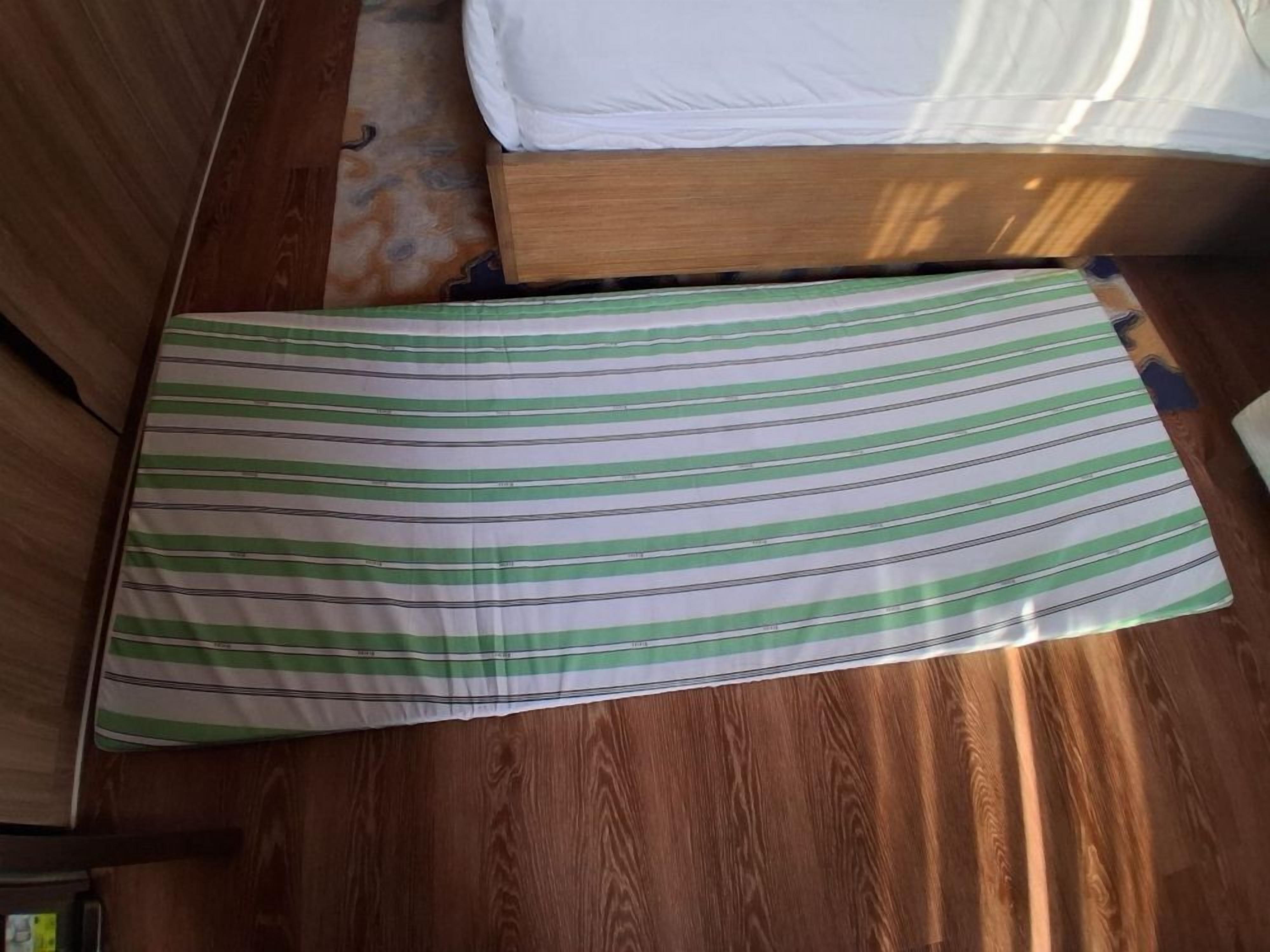 En seng med hvid madras og et stribet tæppe.