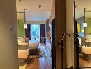 Une chambre d’hôtel comprenant un lit, des tables de chevet, un bureau, une chaise, une salle de bain avec un miroir et une vue sur le paysage urbain.