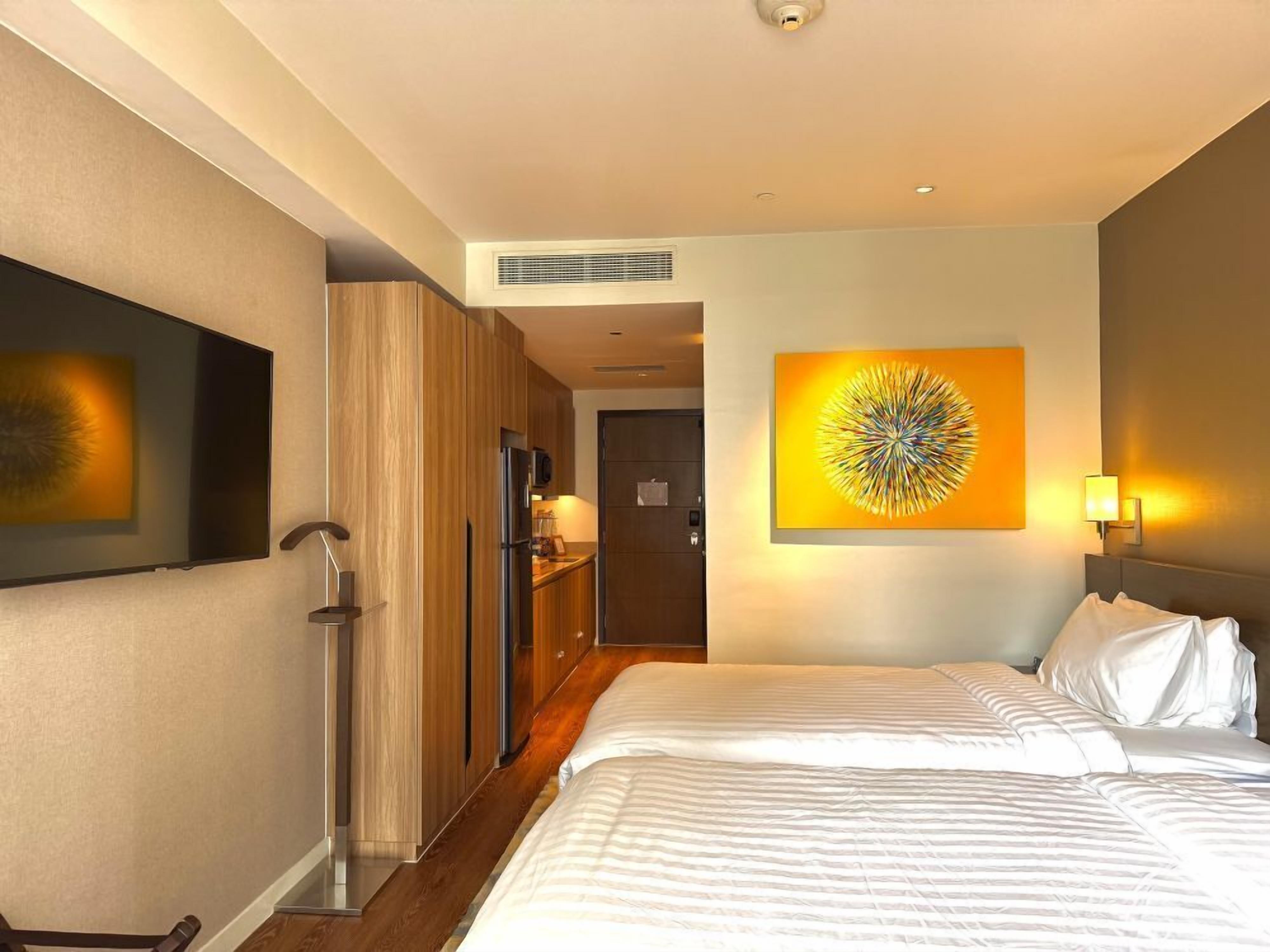 Ein Hotelzimmer mit Bett, Fernseher, Küchenzeile und einem großen Kunstwerk an der Wand.