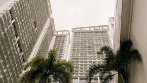 A high-rise building with a grid-like facade, multiple balconies, and a palm tree in the foreground. - Mesmerizing Twin Bed,Rockwell View (Mandaluyong City)