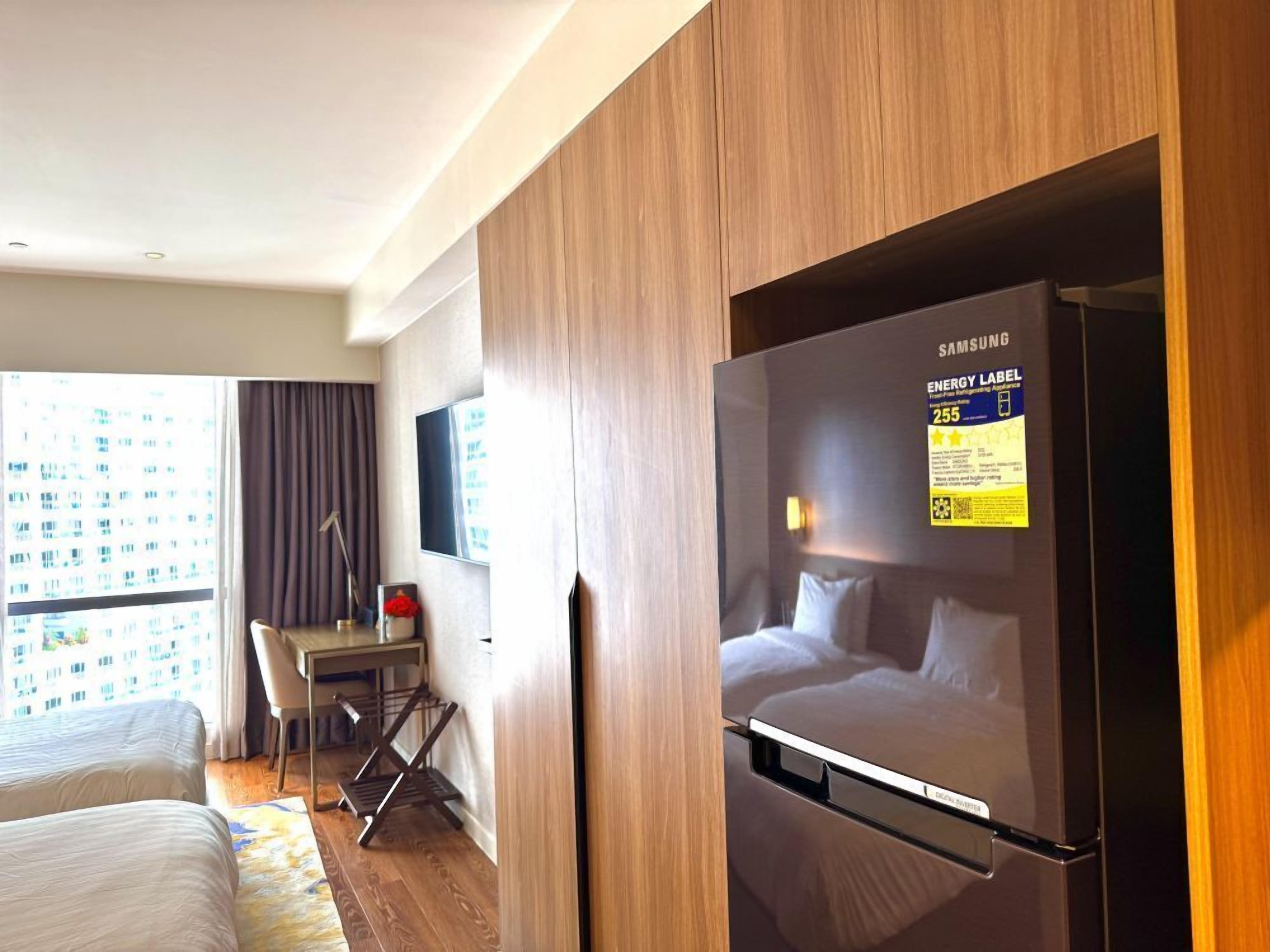 A hotel room with a bed, a desk, a chair, a TV, and a refrigerator.